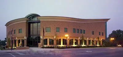 A brick civic building at dusk with its exterior lights on